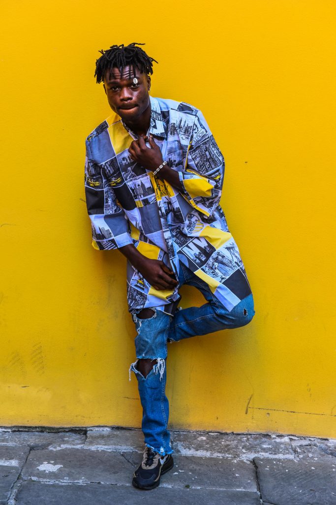 Stylish young man in vibrant urban attire poses against a bold yellow wall.
